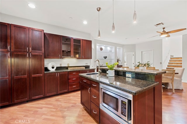 210 N Stage Coach Ln, Fallbrook, CA 92028 - kitchen with stainless steel microwave, dark brown cabinets, decorative light fixtures, light wood-type flooring, and a center island with sink
