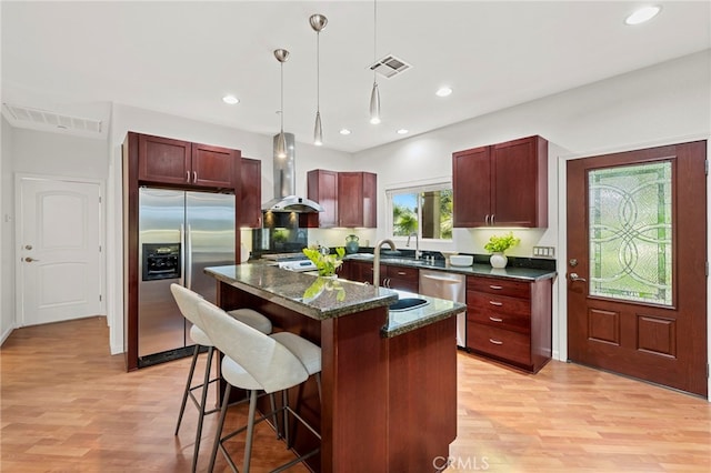 210 N Stage Coach Ln, Fallbrook, CA 92028 - kitchen featuring stainless steel appliances, wall chimney range hood, light wood finished floors, a kitchen bar, and hanging light fixtures