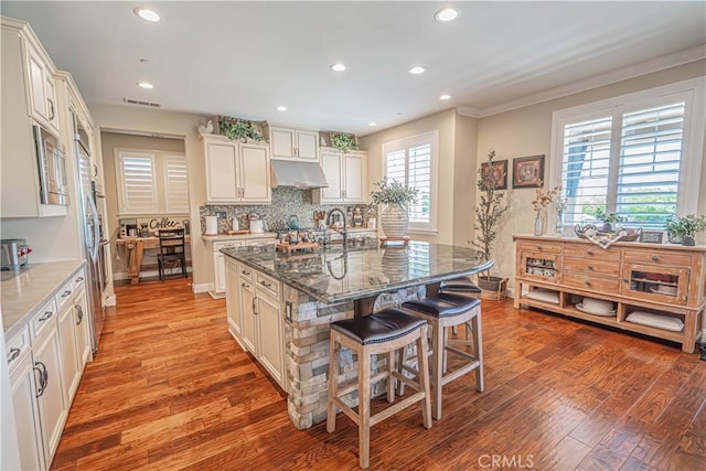 22348 Driftwood Ct, Saugus, CA 91350 - kitchen with a kitchen breakfast bar, under cabinet range hood, light wood finished floors, dark stone counters, and recessed lighting