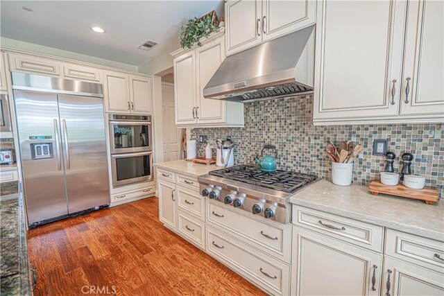 22348 Driftwood Ct, Saugus, CA 91350 - kitchen with appliances with stainless steel finishes, range hood, light wood-style flooring, and decorative backsplash