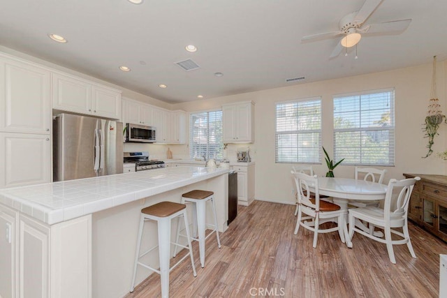 1133 Maag Pl Unit 107, Fullerton, CA 92833 - kitchen featuring appliances with stainless steel finishes, white cabinetry, light wood-style floors, ceiling fan, and a breakfast bar