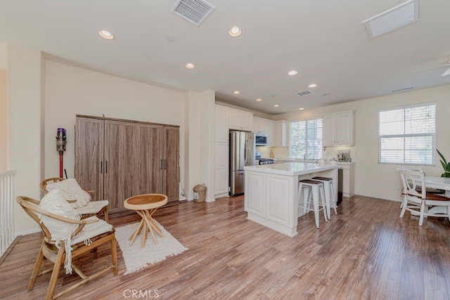 1133 Maag Pl Unit 107, Fullerton, CA 92833 - kitchen featuring appliances with stainless steel finishes, a kitchen island, a breakfast bar, white cabinetry, and light wood-style flooring