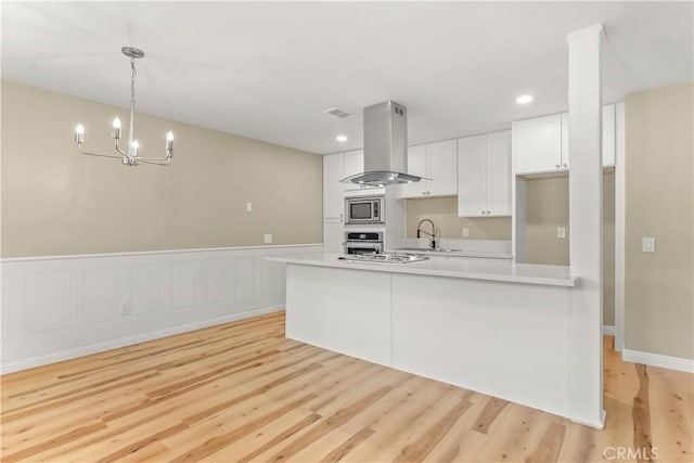 1446 Morgan Rd, San Bernardino, CA 92407 - kitchen featuring island exhaust hood, appliances with stainless steel finishes, white cabinetry, light countertops, and light wood-type flooring