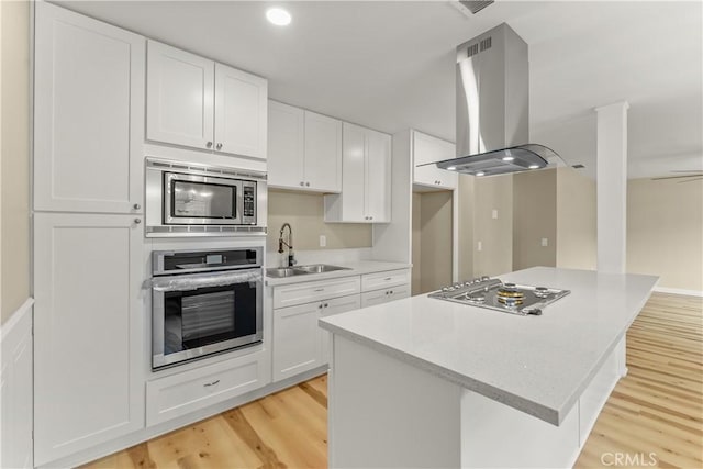 1446 Morgan Rd, San Bernardino, CA 92407 - kitchen with appliances with stainless steel finishes, island exhaust hood, light wood-style floors, light countertops, and white cabinets