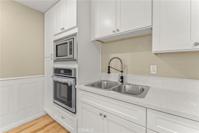 1446 Morgan Rd, San Bernardino, CA 92407 - kitchen with stainless steel appliances, white cabinetry, light wood-style floors, wainscoting, and light stone countertops