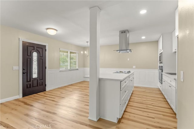 1446 Morgan Rd, San Bernardino, CA 92407 - kitchen featuring island range hood, light wood-style floors, white cabinetry, a wainscoted wall, and appliances with stainless steel finishes