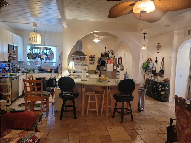 15845 La Vida Dr, Palm Springs, CA 92262 - bar area with wall chimney exhaust hood, ceiling fan, stone tile floors, arched walkways, and appliances with stainless steel finishes