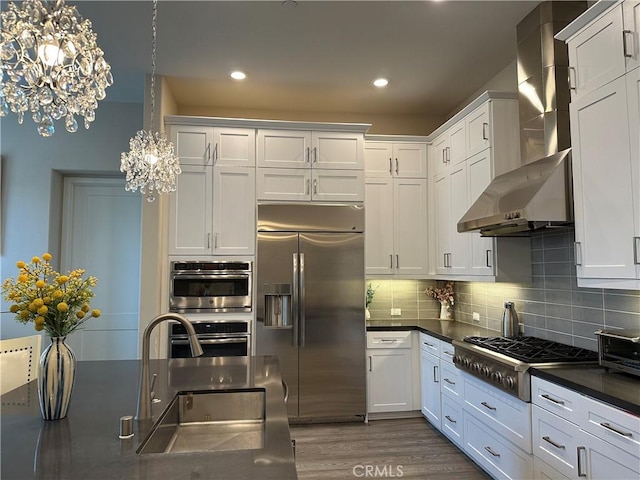 227 Carlow, Irvine, CA 92618 - kitchen featuring appliances with stainless steel finishes, wall chimney range hood, a chandelier, dark countertops, and white cabinetry