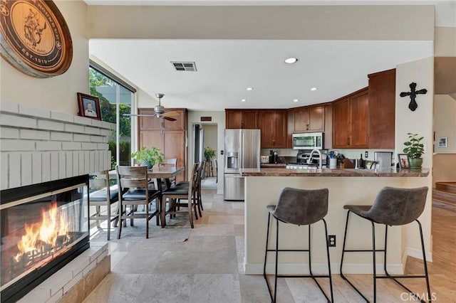 15736 Milne Cir, Moorpark, CA 93021 - kitchen featuring appliances with stainless steel finishes, a fireplace, ceiling fan, a peninsula, and a kitchen bar