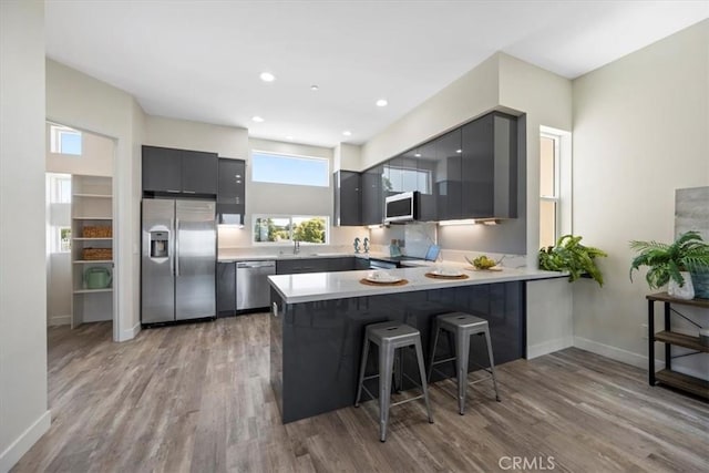 1296 Saratoga Ave, Grover Beach, CA 93433 - kitchen with appliances with stainless steel finishes, a peninsula, modern cabinets, light wood finished floors, and a breakfast bar