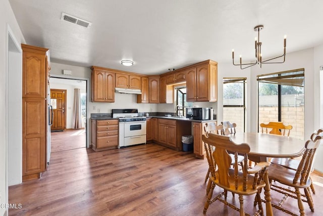 236 S 11th St, Santa Paula, CA 93060 - kitchen with white gas range oven, a chandelier, wood finished floors, dark countertops, and under cabinet range hood
