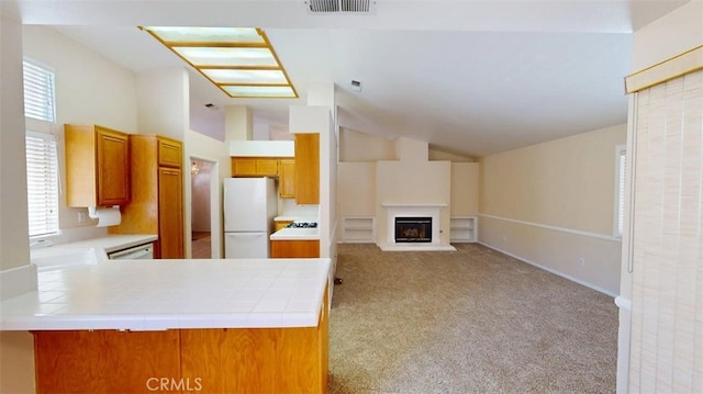 12429 Pocono Pl, Apple Valley, CA 92308 - kitchen featuring freestanding refrigerator, vaulted ceiling, light colored carpet, brown cabinets, and a glass covered fireplace