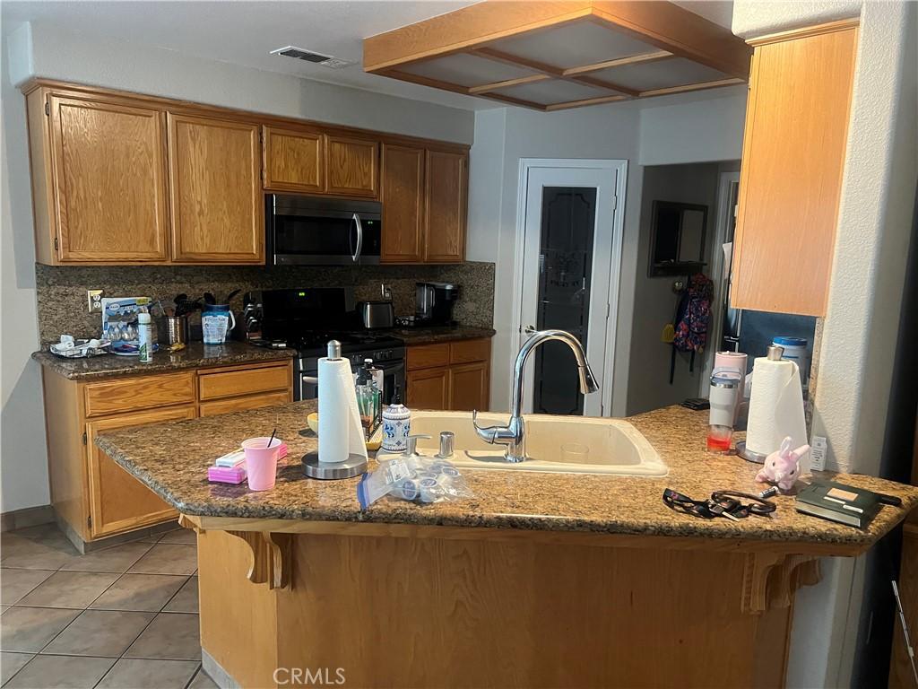 757 Nighthawk Ct, Merced, CA 95340 - kitchen with appliances with stainless steel finishes, a peninsula, decorative backsplash, a kitchen bar, and light tile patterned floors