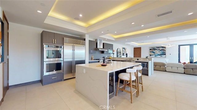 12480 Viewcrest Rd, Studio City, CA 91604 - kitchen with built in appliances, a raised ceiling, wall chimney range hood, modern cabinets, and a large island with sink