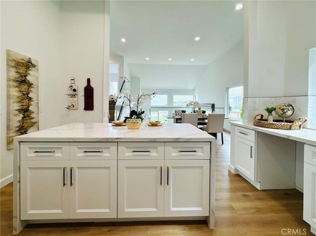 83 Palm Beach Ct, Dana Point, CA 92629 - kitchen featuring light wood-style flooring, light stone counters, white cabinets, lofted ceiling, and decorative backsplash