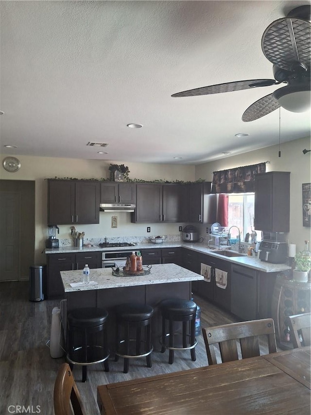 13772 Helena Ave, Victorville, CA 92392 - kitchen with dark wood finished floors, stainless steel gas cooktop, a ceiling fan, a kitchen island, and a kitchen bar