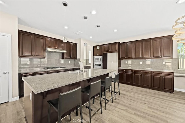 6792 Vanderbilt St, Chino, CA 91710 - kitchen featuring under cabinet range hood, appliances with stainless steel finishes, light wood-style floors, tasteful backsplash, and hanging light fixtures