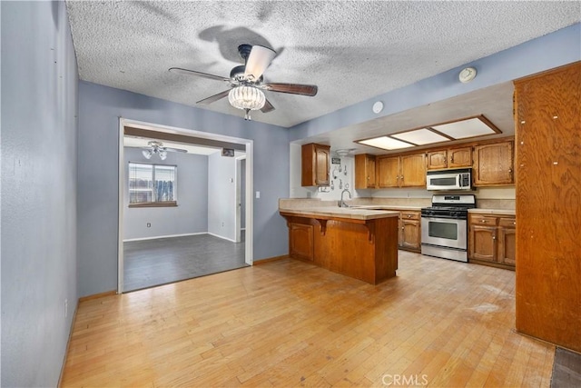 5013 Stancliff St, Bakersfield, CA 93307 - kitchen featuring stainless steel gas stove, brown cabinetry, a peninsula, a kitchen bar, and light countertops