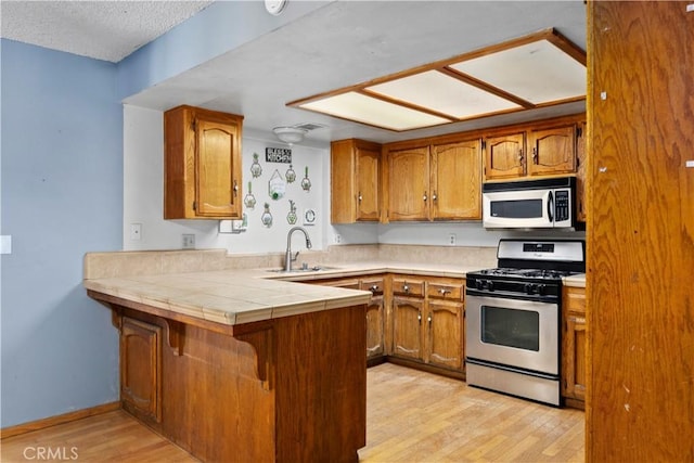 5013 Stancliff St, Bakersfield, CA 93307 - kitchen with stainless steel range with gas cooktop, a peninsula, brown cabinetry, and light wood-style floors