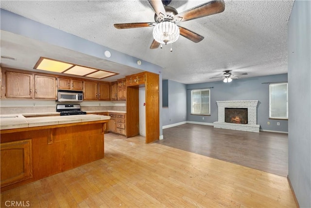 5013 Stancliff St, Bakersfield, CA 93307 - kitchen featuring stainless steel appliances, a ceiling fan, brown cabinetry, a textured ceiling, and light wood-style flooring