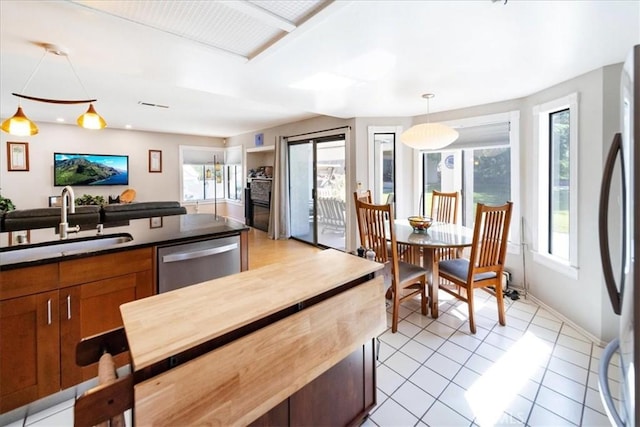 5963 Rio Valle Dr, Bonsall, CA 92003 - kitchen featuring stainless steel dishwasher, dark countertops, light tile patterned floors, refrigerator, and hanging light fixtures
