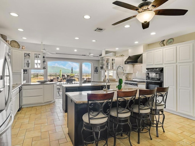 31755 Rancho Vista Rd, Temecula, CA 92592 - kitchen featuring a ceiling fan, a kitchen island with sink, wall chimney exhaust hood, a kitchen bar, and recessed lighting