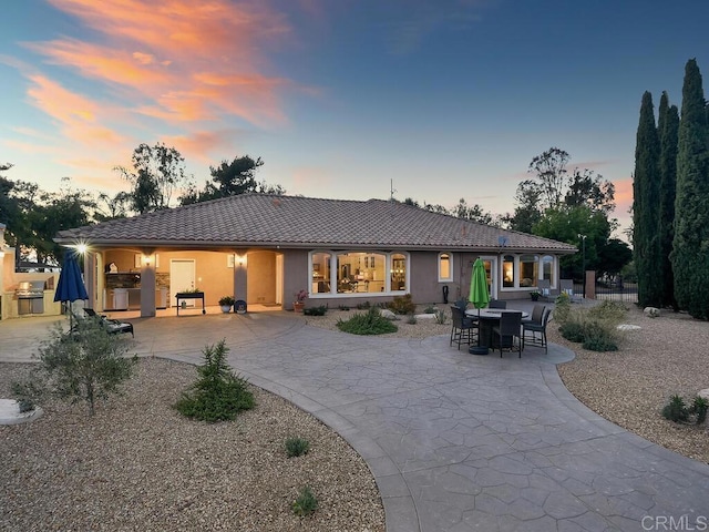 31755 Rancho Vista Rd, Temecula, CA 92592 - back of house at dusk with a patio area, a tile roof, stucco siding, curved driveway, and an outdoor kitchen