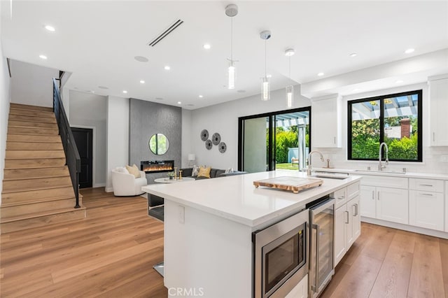 251 S Griffith Park Dr, Burbank, CA 91506 - kitchen featuring wine cooler, stainless steel microwave, a center island with sink, light wood-style floors, and recessed lighting