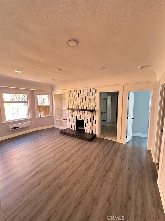 696 E 51st St E, Los Angeles, CA 90011 - unfurnished living room featuring a textured ceiling, dark wood finished floors, a stone fireplace, built in shelves, and an AC wall unit