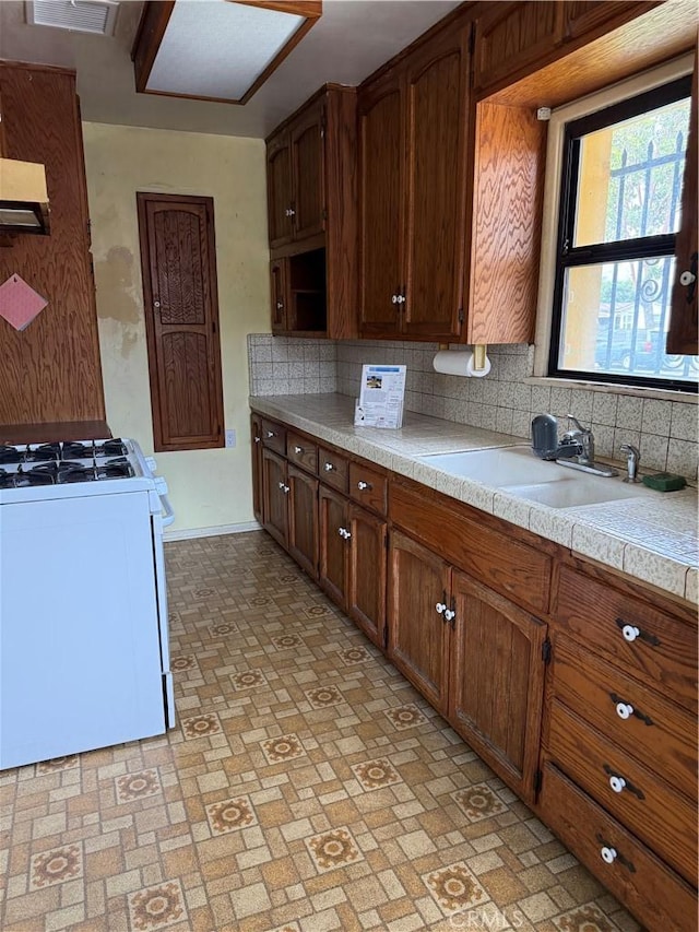 1317 S Baker St, Santa Ana, CA 92707 - kitchen with white gas range, light countertops, backsplash, ventilation hood, and brick patterned flooring