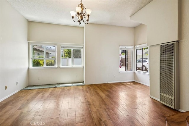 1263 Pismo St, San Luis Obispo, CA 93401 - empty room with a heating unit, a chandelier, healthy amount of natural light, wood-type flooring, and a textured ceiling