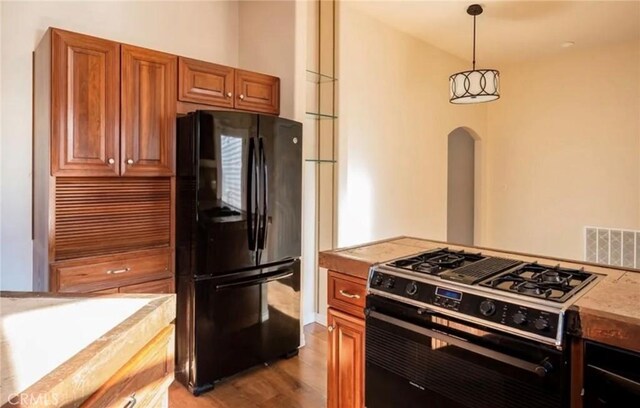 1263 Pismo St, San Luis Obispo, CA 93401 - kitchen featuring black appliances, arched walkways, light wood finished floors, brown cabinetry, and pendant lighting