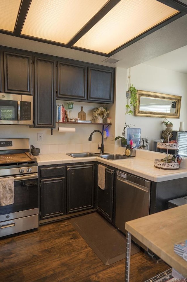 29517 Cara Way, Temecula, CA 92591 - kitchen with appliances with stainless steel finishes, dark wood-style floors, tile counters, open shelves, and a peninsula