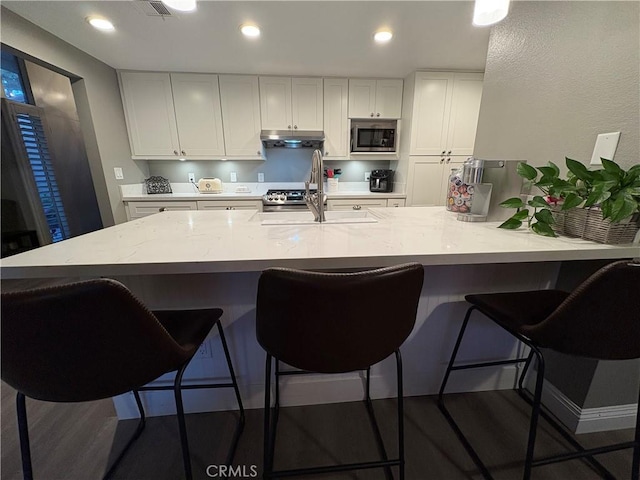 1137 Mountain Gate Rd, Upland, CA 91786 - kitchen with stainless steel microwave, under cabinet range hood, white cabinets, wood finished floors, and recessed lighting