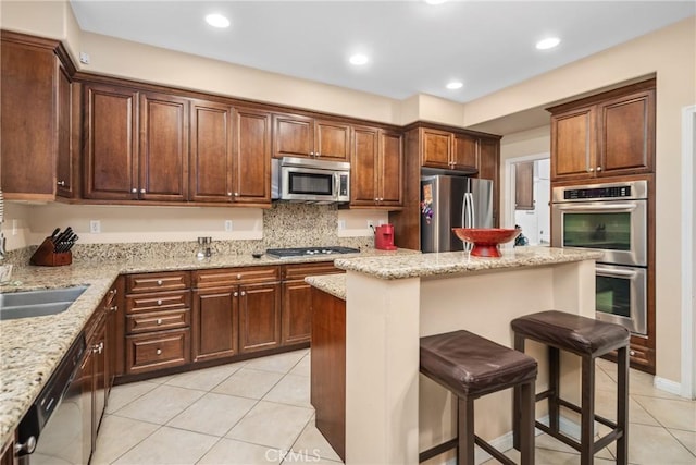7116 W W Ave L4, Lancaster, CA 93536 - kitchen with stainless steel appliances, light tile patterned floors, a breakfast bar, light stone counters, and a center island