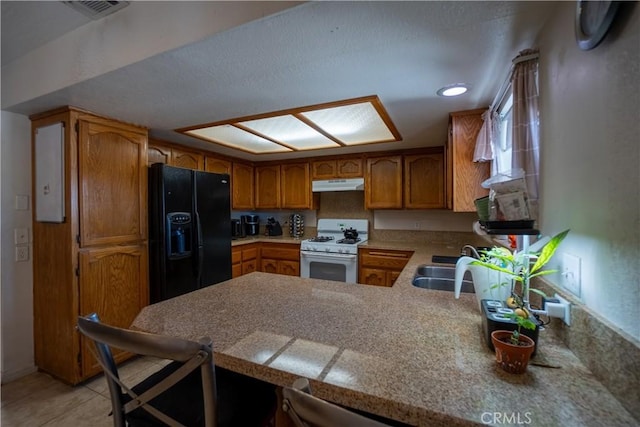 7681 Newhall Ave, Hesperia, CA 92345 - kitchen featuring black fridge, white gas stove, under cabinet range hood, a peninsula, and brown cabinetry