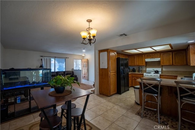 7681 Newhall Ave, Hesperia, CA 92345 - kitchen with white range with gas cooktop, under cabinet range hood, black refrigerator with ice dispenser, brown cabinetry, and a chandelier