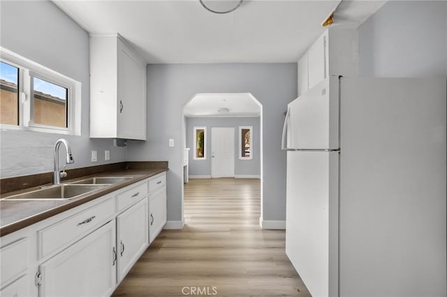 1163 W 3rd St, Pomona, CA 91766 - kitchen with freestanding refrigerator, dark countertops, white cabinetry, light wood finished floors, and arched walkways