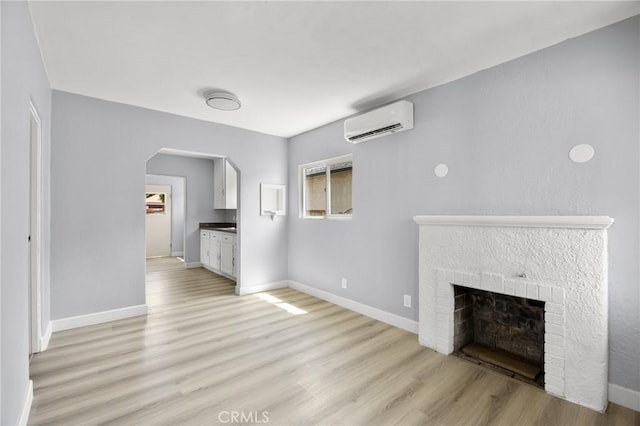 1163 W 3rd St, Pomona, CA 91766 - unfurnished living room with a wall unit AC, light wood-style flooring, a fireplace, arched walkways, and plenty of natural light