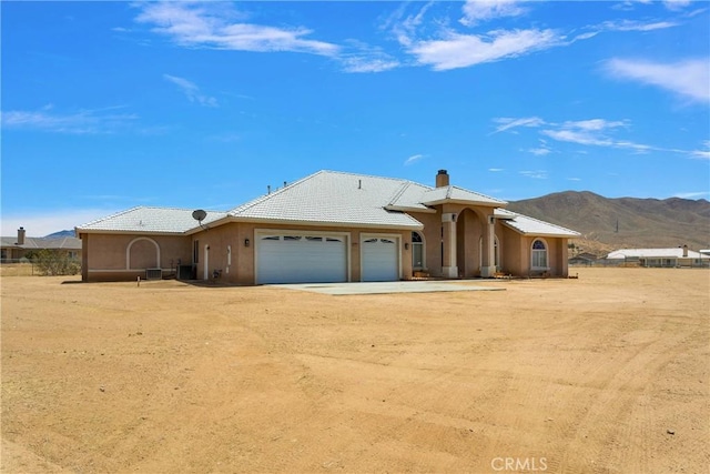 21777 Poppy Rd, Apple Valley, CA 92308 - view of front of property featuring an attached garage, a mountain view, dirt driveway, a chimney, and stucco siding