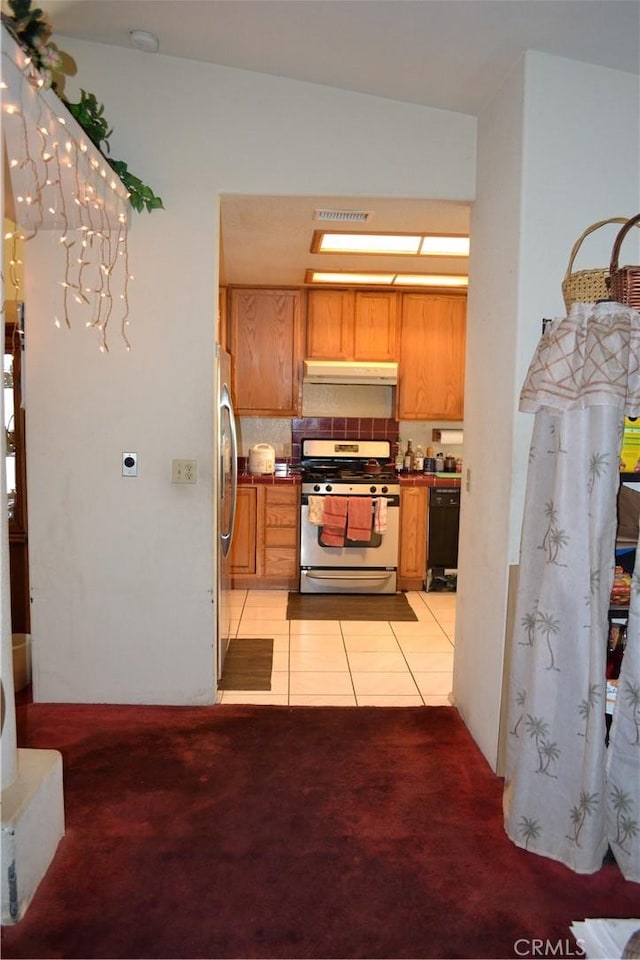 31811 Whispering Palms Trl, Cathedral City, CA 92234 - kitchen with gas range oven, freestanding refrigerator, under cabinet range hood, light colored carpet, and light tile patterned floors