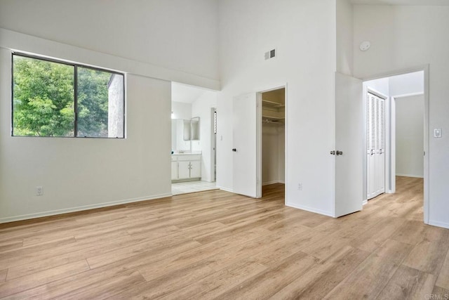 2315 Nicklaus Dr, Oceanside, CA 92056 - unfurnished bedroom with a towering ceiling, light wood-type flooring, multiple windows, a spacious closet, and connected bathroom