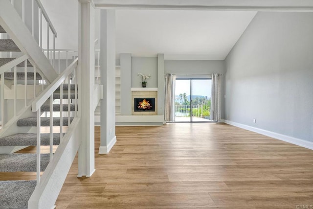 2315 Nicklaus Dr, Oceanside, CA 92056 - unfurnished living room with vaulted ceiling, wood finished floors, stairs, and a warm lit fireplace