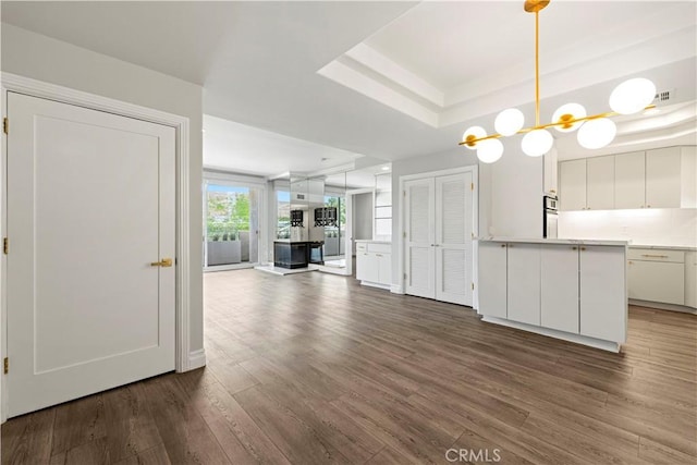 390 S Sepulveda Blvd Unit 105, Los Angeles, CA 90049 - unfurnished living room featuring dark wood finished floors, a tray ceiling, and a chandelier