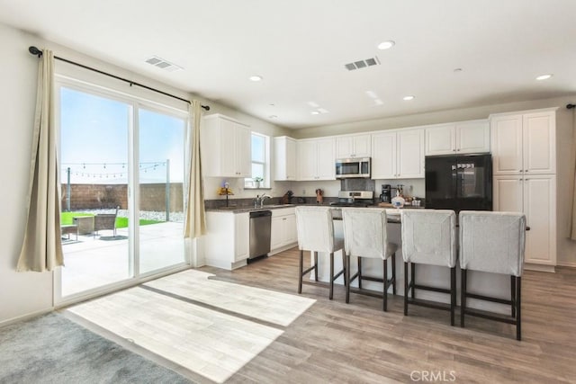 13343 Macaw Pl, Victorville, CA 92395 - kitchen with stainless steel appliances, white cabinetry, a breakfast bar area, light wood-type flooring, and a center island