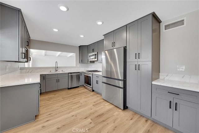 1106 W Bellbrook St, Covina, CA 91722 - kitchen featuring appliances with stainless steel finishes, gray cabinetry, light stone counters, light wood-style flooring, and recessed lighting