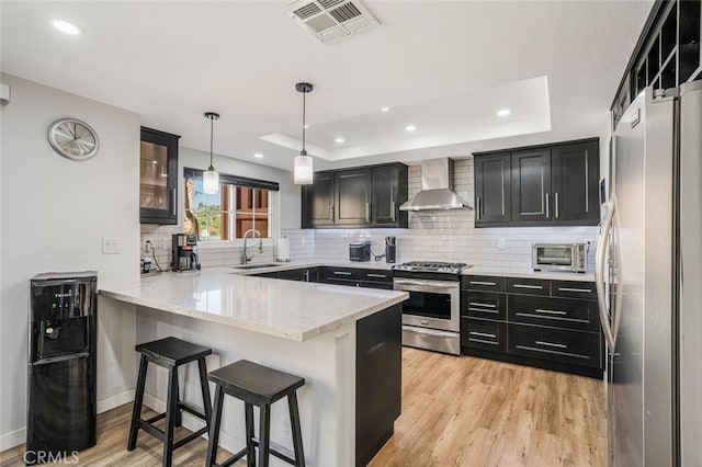 4347 Freedom Dr Unit C, Calabasas, CA 91302 - kitchen with appliances with stainless steel finishes, wall chimney range hood, a peninsula, a raised ceiling, and dark cabinetry