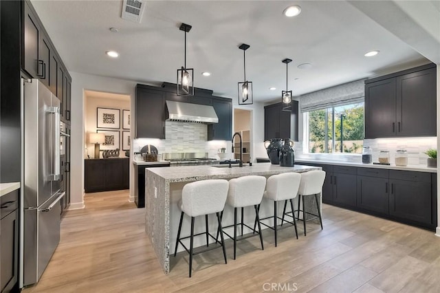 3042 Mesa Gln, Escondido, CA 92026 - kitchen with appliances with stainless steel finishes, ventilation hood, a kitchen island with sink, tasteful backsplash, and recessed lighting