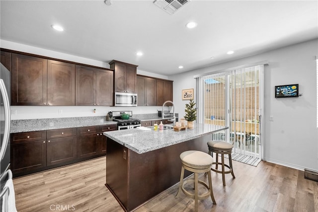 5609 Garibaldi Way, Fontana, CA 92336 - kitchen featuring stainless steel appliances, light wood-style flooring, a kitchen breakfast bar, a center island with sink, and light stone counters