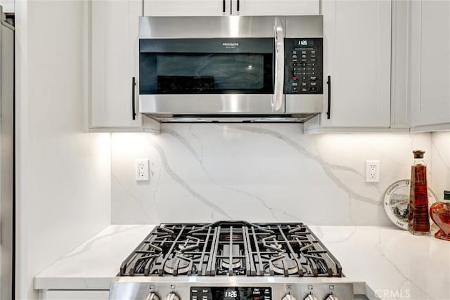 25072 Leucadia St Unit E, Laguna Niguel, CA 92677 - kitchen view of stainless steel microwave, backsplash, gas range oven, light stone countertops, and white cabinets